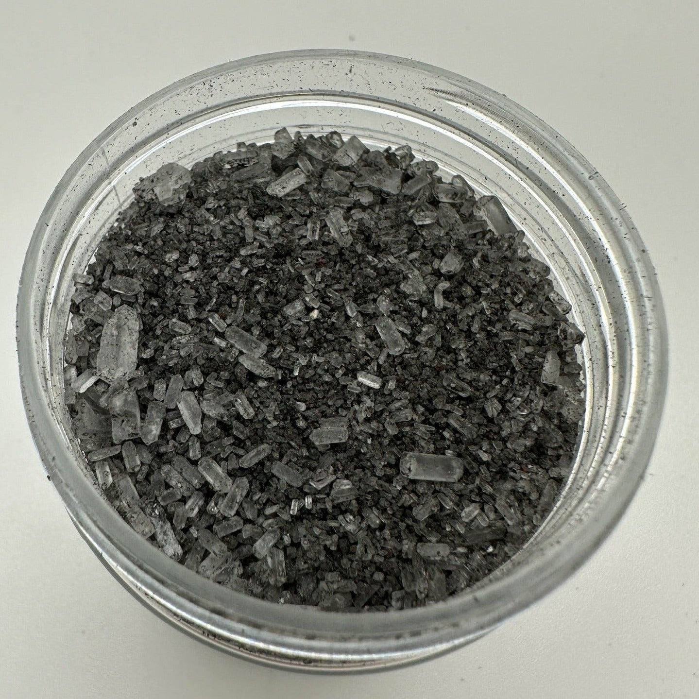 Black colored bath salts in a clear jar that is open