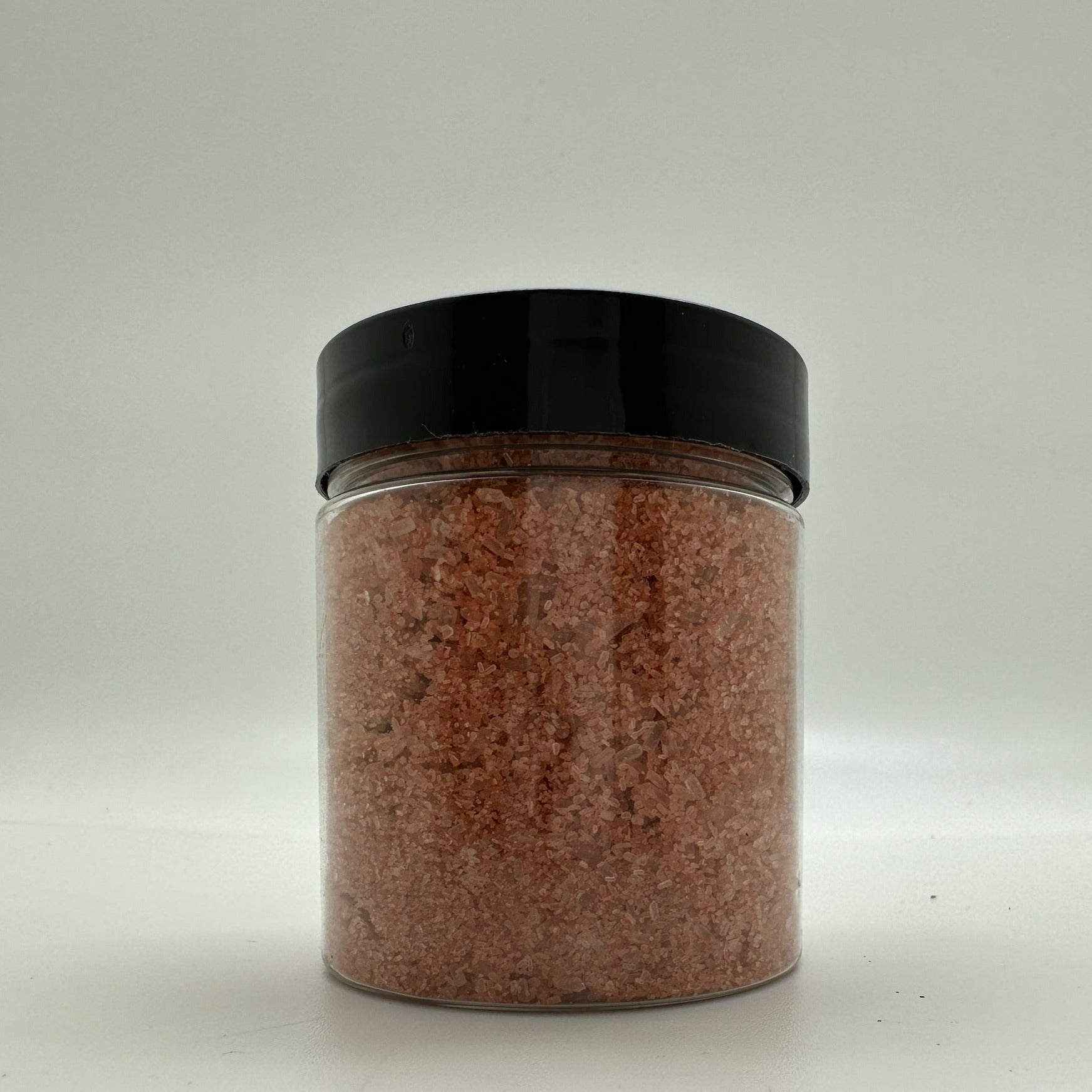 Red colored bath salts in clear jar with black lid.