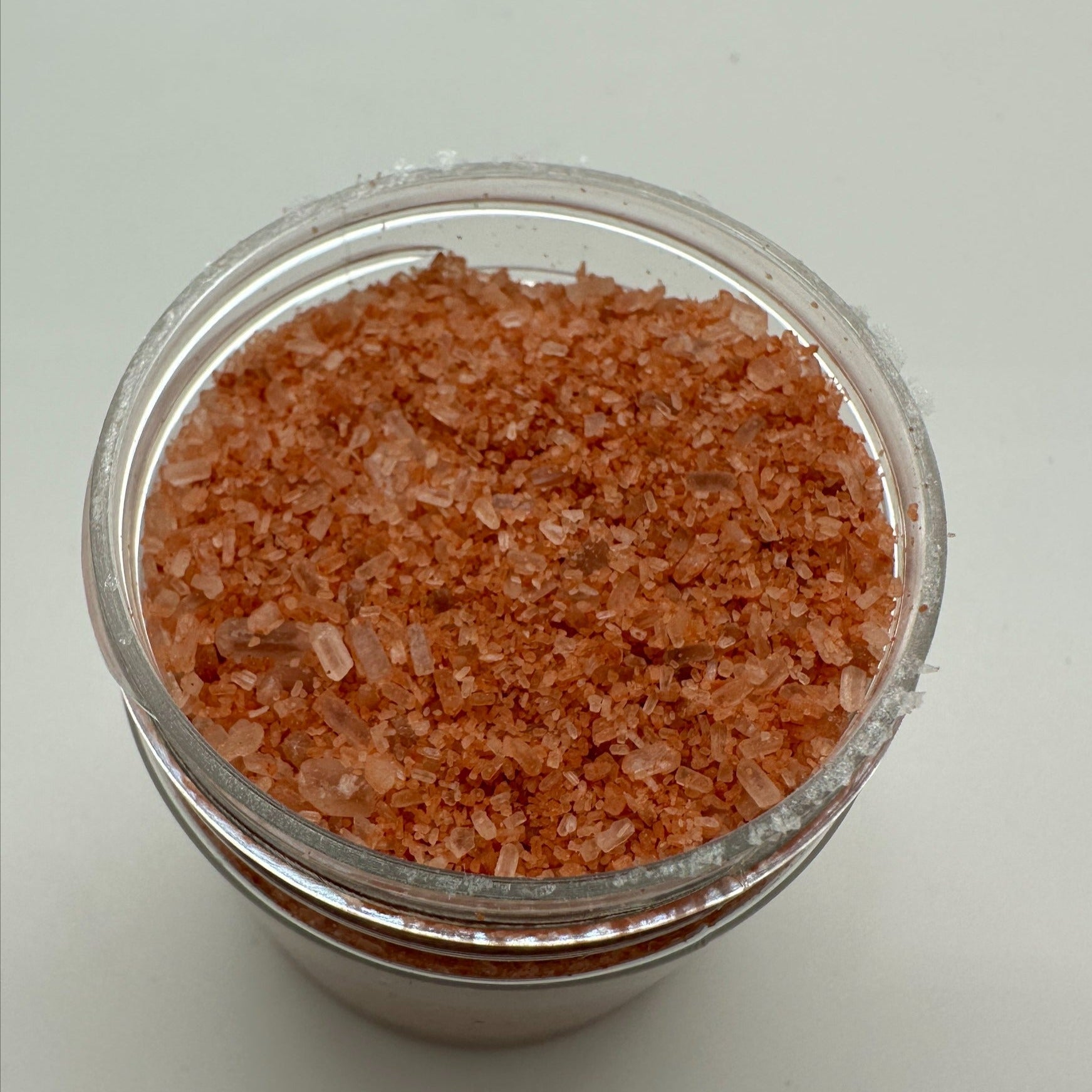 Red colored bath salts in a clear jar that is open.